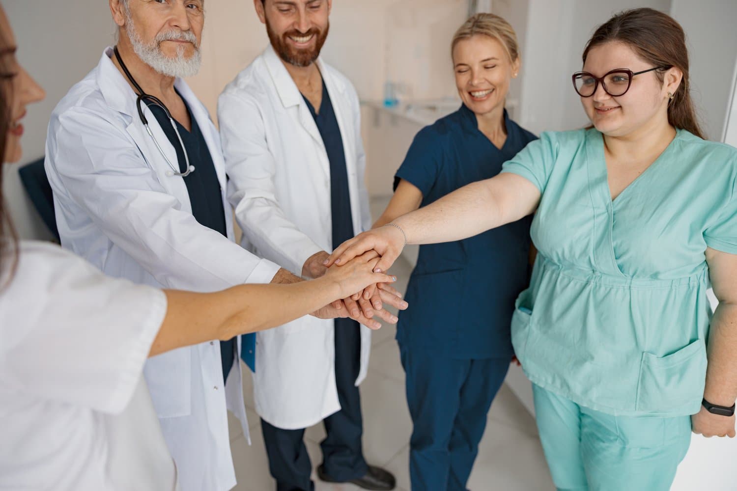 Group of professional medical team of doctors putting their hands together standing in clinic